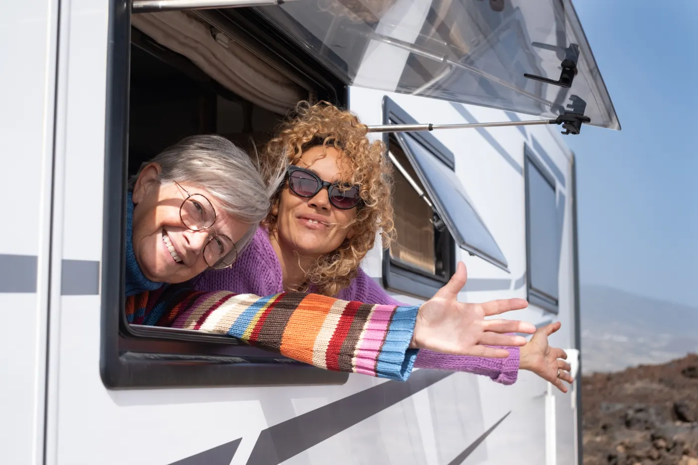 Two smiling women waving from the window of their RV